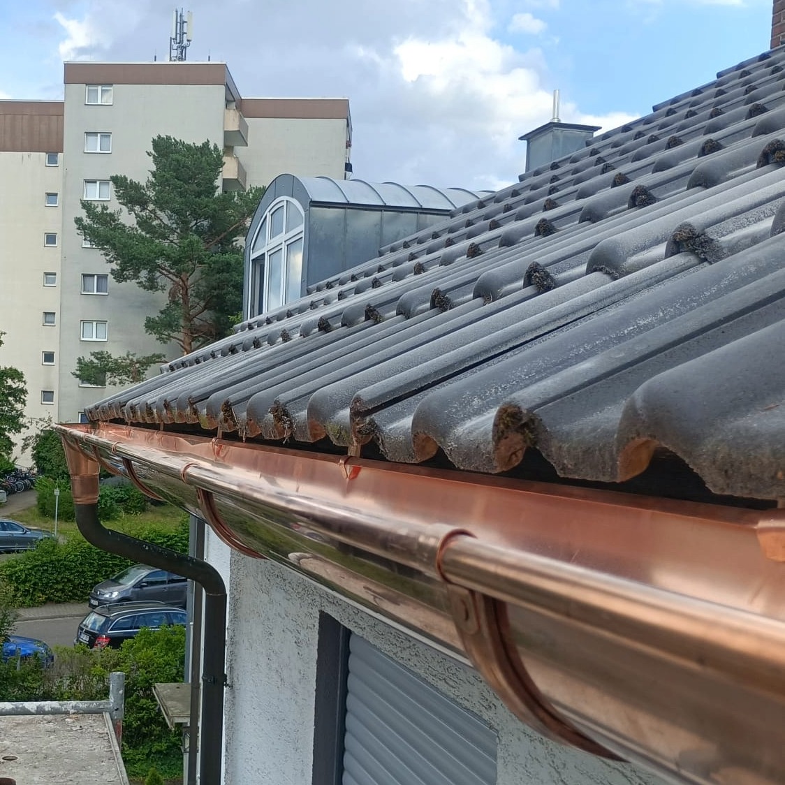 Neu montierte, glänzende Kupfer-Dachrinne an einem Wohnhaus mit dunklen Dachziegeln